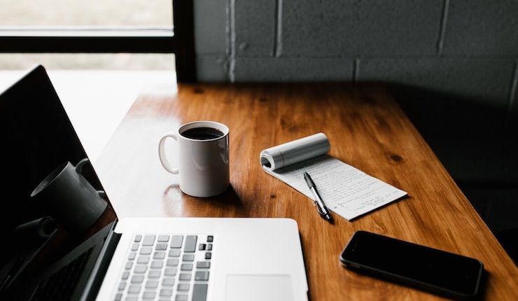 MacBook Pro, white ceramic mug,and black smartphone on table