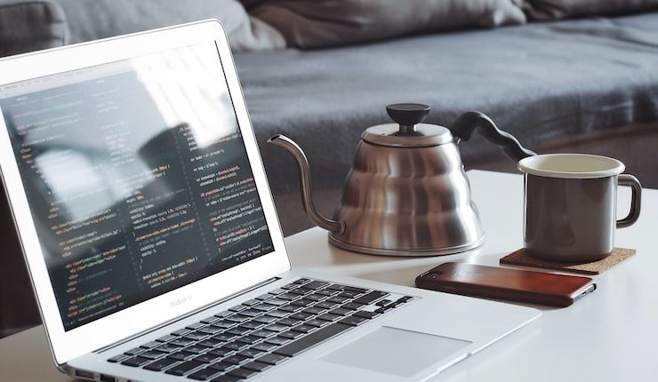 turned on MacBook Air beside black smartphone and black ceramic mug